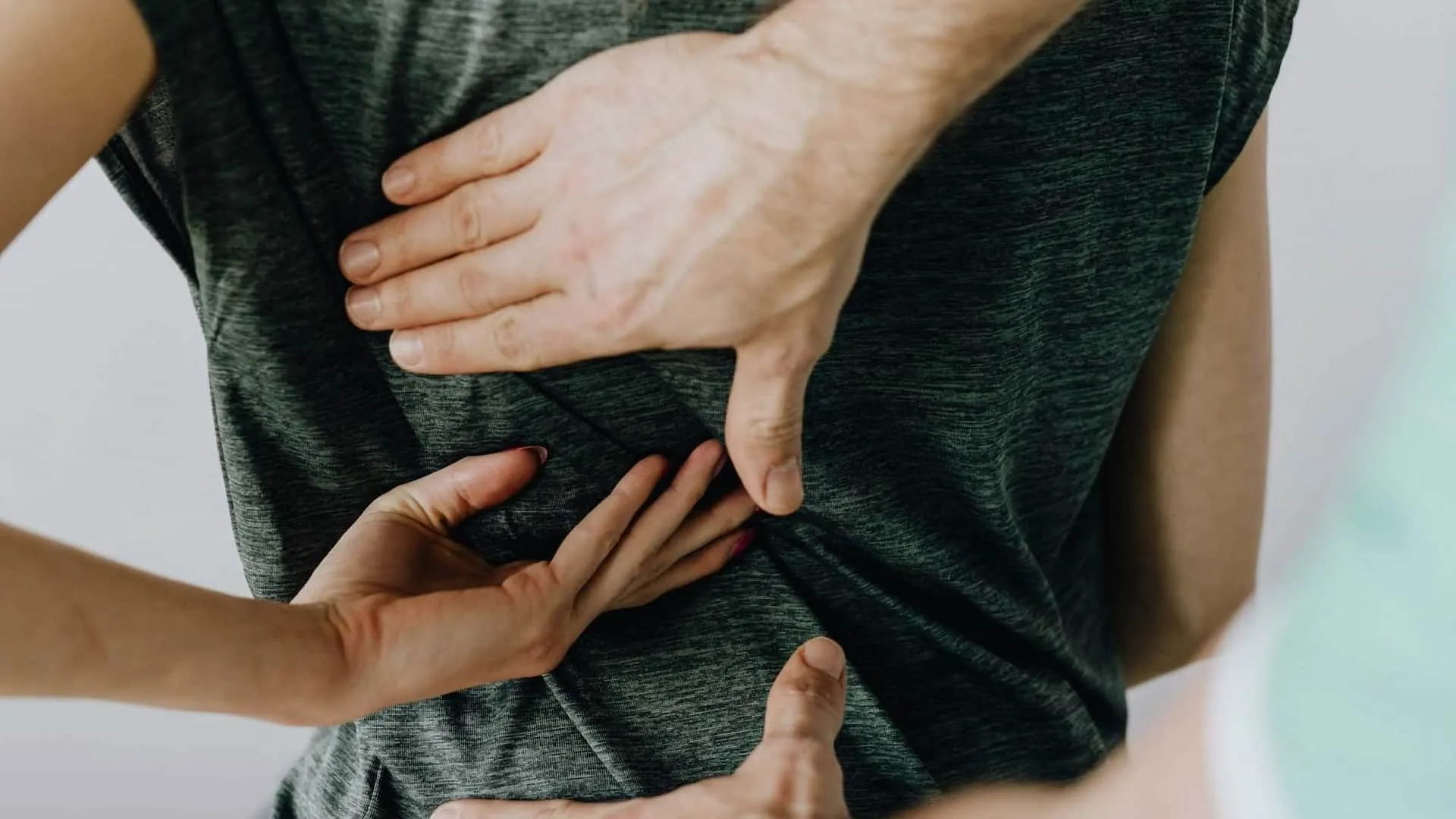 Close-up of multiple hands touching a person's back, who is wearing a grey t-shirt.