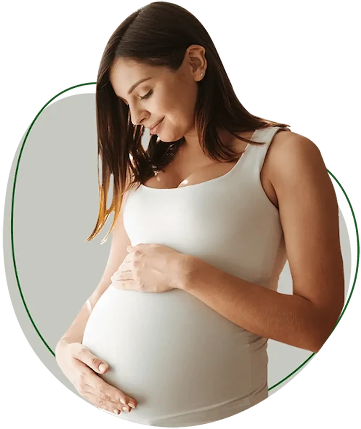 A pregnant woman in a white tank top gently holds her belly and looks down with a soft smile.