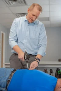 A male chiropractor uses an adjustment tool on a male patient's lower back.