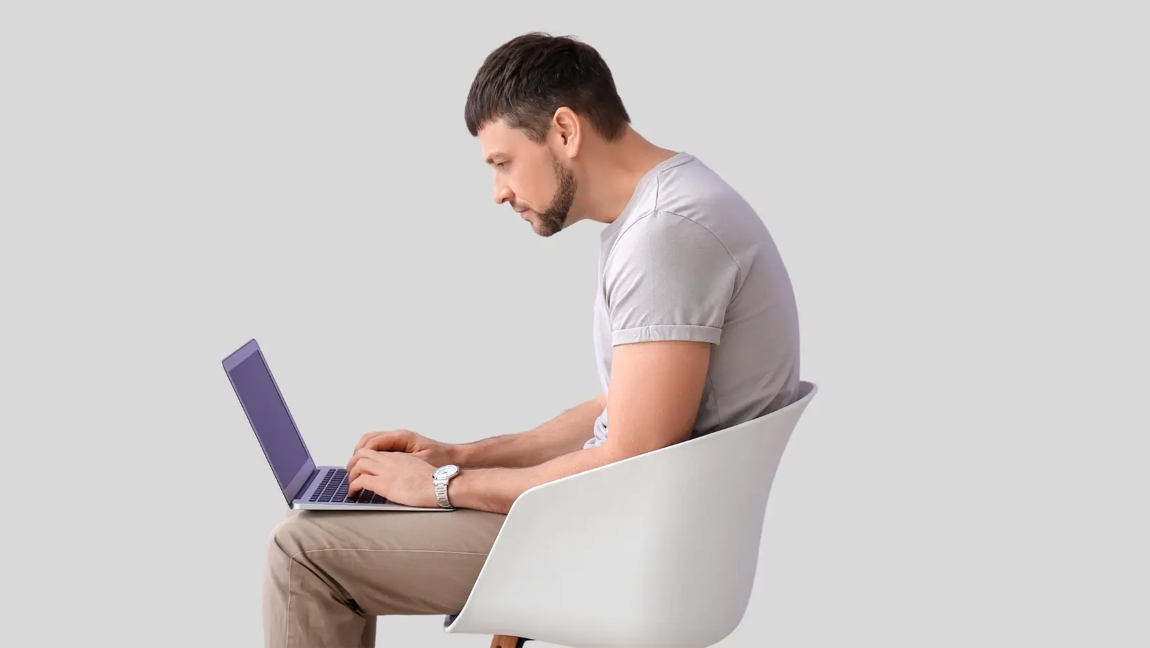 Side profile of a man with poor posture, leaning forward while typing on a laptop on his lap.