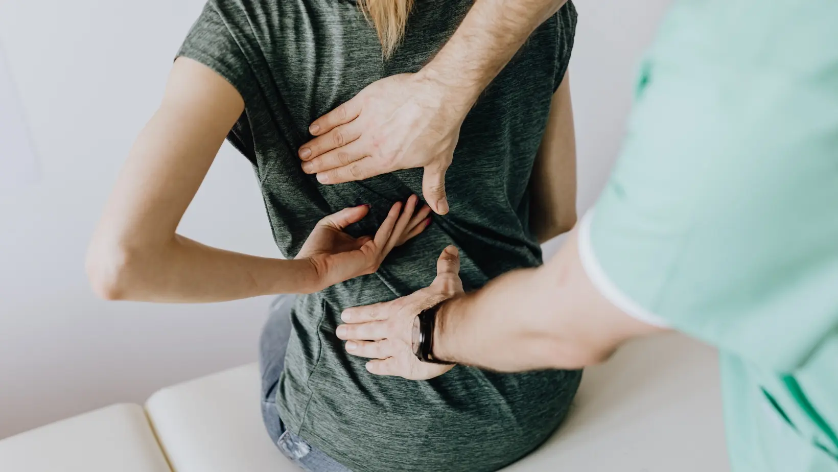 Patient sitting down, facing away from the camera with their left hand behind their back in the middle. The practitioner's hands are located just above and below the patient's.