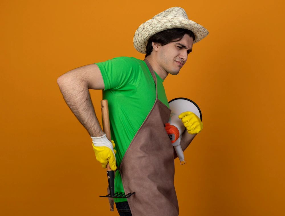 Person gardening and bending while experiencing lower back strain outdoors