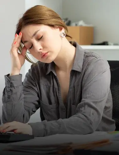 Gateway to Wellness - Home page - Headaches image. Woman sitting at a desk with one hand on a keyboard and the other rubbing against her forehead in discomfort.