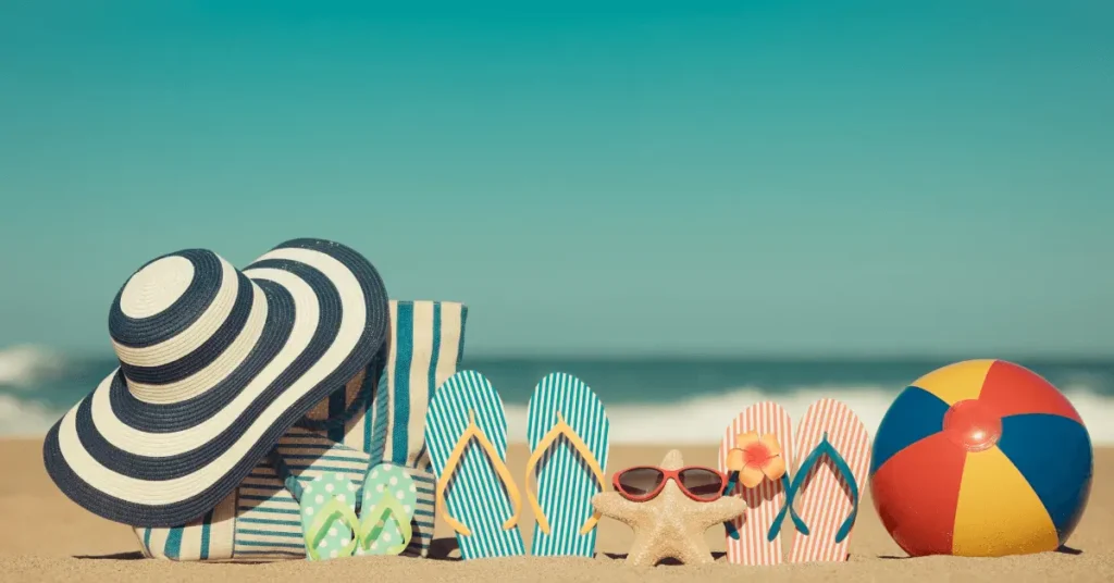 Beach scene with a striped hat, beach bag, three pairs of flip-flops, a starfish with sunglasses, and a colorful beach ball on sand, with the ocean and blue sky in the background.