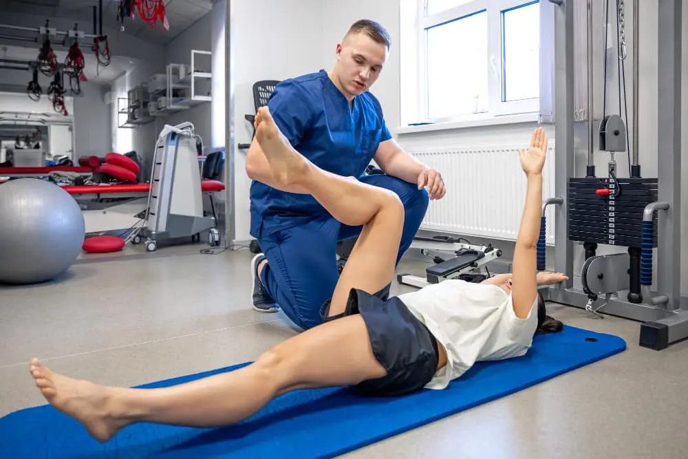 Chiropractic patient performing knee exercises laying on a mat next to the clinician.