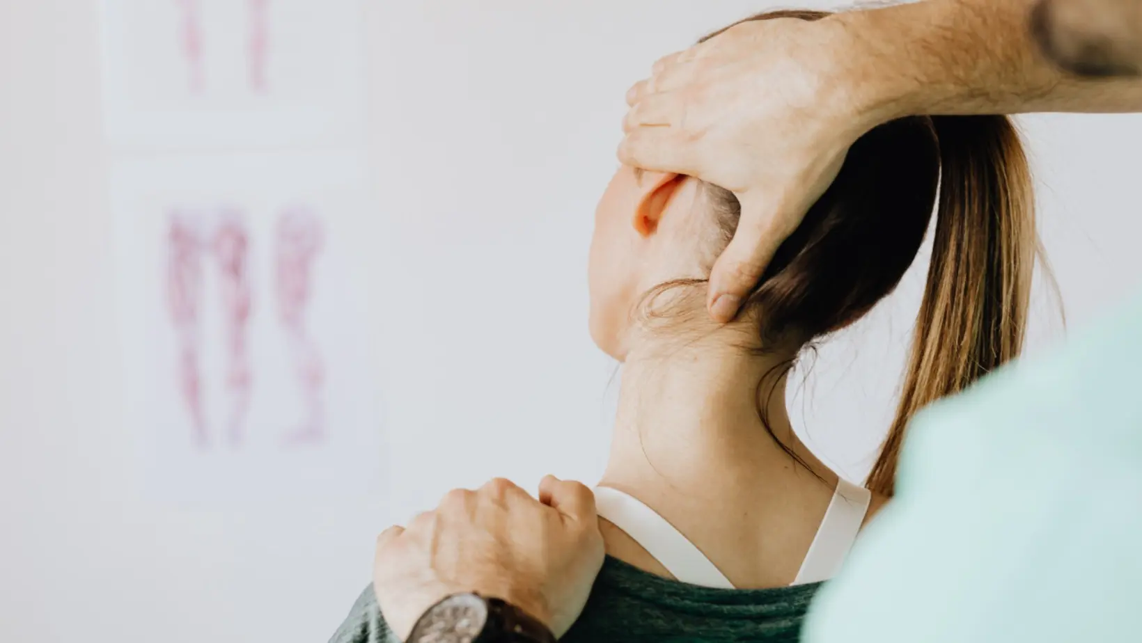 Patient sitting down facing away from the camera. Practitioner has one hand on the left side of her head, gently pushing. His other hand is placed on her left shoulder, holding it in place.