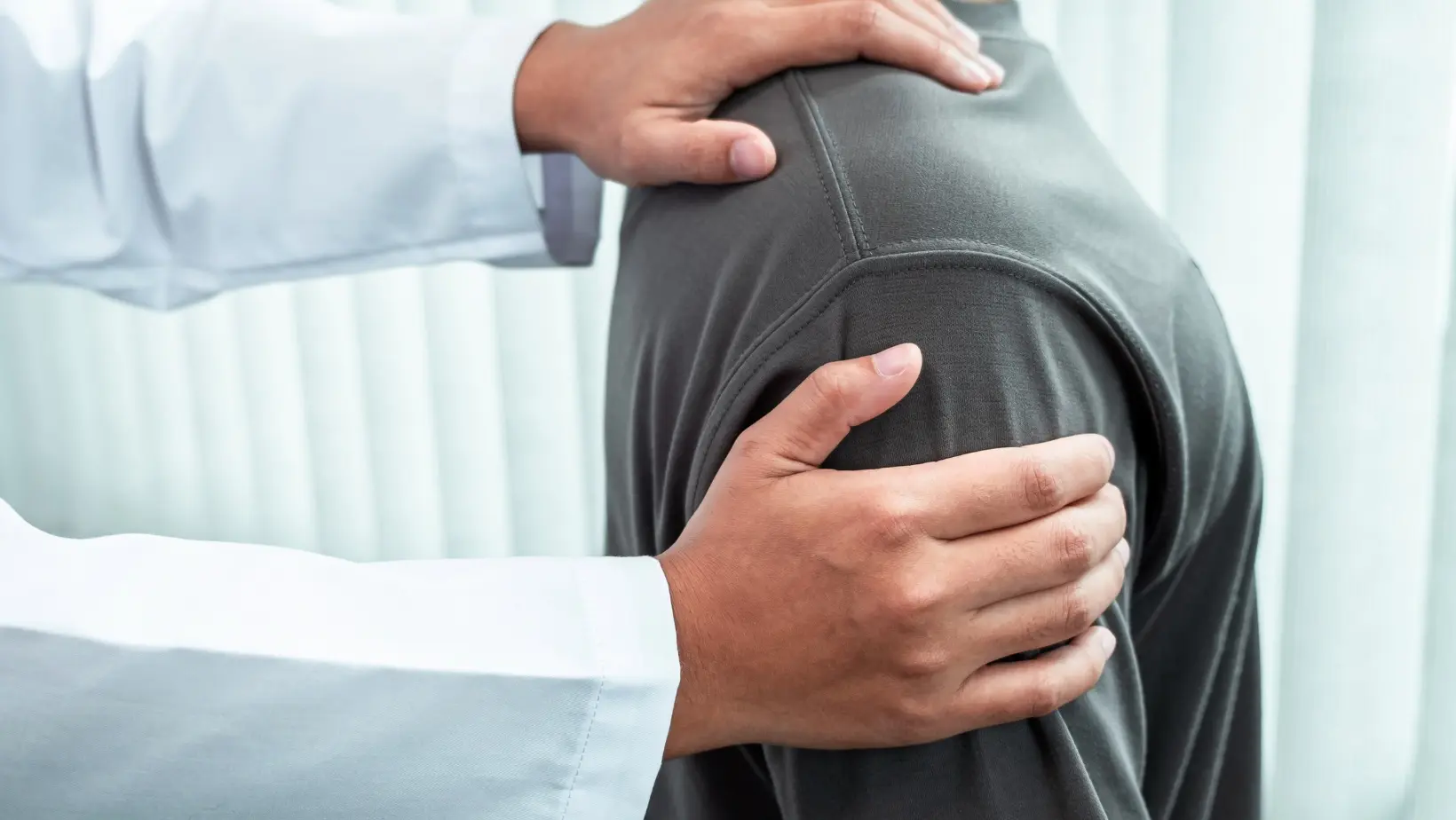 Close-up of a patient's shoulder. Practitioner has his left hand placed on his shoulder, and his right hand placed on his upper arm.